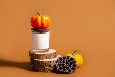 Autumn composition with pumpkin, candle in cup on brown background and hard shadow. Cozy home decor for Halloween or Thanksgiving day. Mockupの写真素材