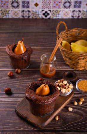 Sweet homemade chocolate biscuit mini pie in cup with whole pear and nuts on wooden tableの写真素材