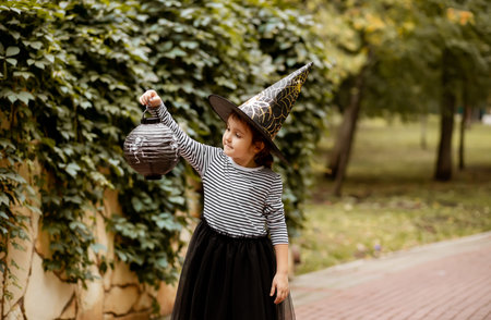 Little cute girl in witch costume holding paper lantern. Kid having fun on Halloween holidayの写真素材