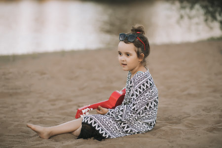 Happy cute little girl child playing guitar nearby lake or river on nature background.の写真素材