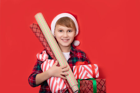 Cute caucasian kid teenager boy in Santa hat holds gift boxes with wrapping papers on red background. Copy space for design or text. Banner. Christmas New Year mockup template.の写真素材