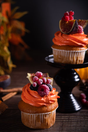Delicious homemade autumn season spicy pumpkin cupcakes with whipped orange cream with fruit figs and frozen berriesの写真素材