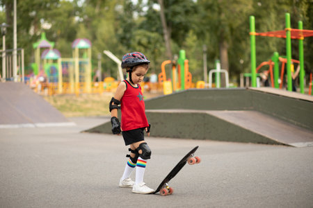 Cute kid girl child with skateboard in a hands standing in a skatepark and smiling. Child performs tricks. Summer sport activity concept. happy childhood.の写真素材