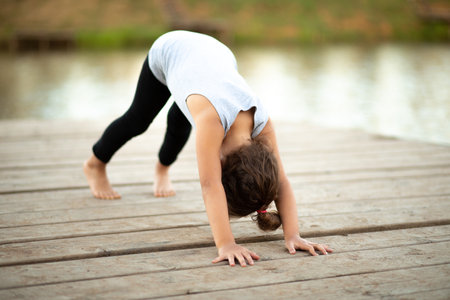 Llittle girl sitting in nature near by river or lake and practicing yoga. healthy lifestyleの写真素材