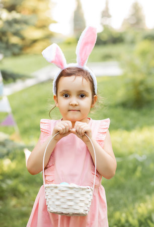 Little cute girl wear bunny ears holding basket with colorful painted eggs on Easter egg hunt in parkの写真素材