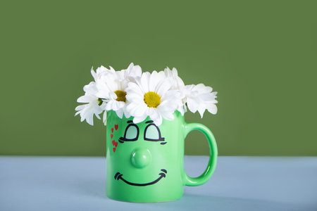 Bouquet of chamomile in green cup with funny face. Greeting postcard.の写真素材