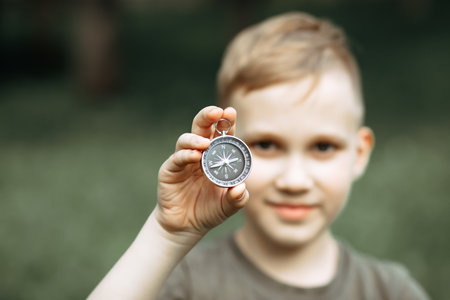 Caucasian cute kid boy with a backpack travels with a compass. Child boy scout holding in a hand...