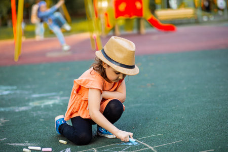 Little cute happy girl draws painting a chalk on pavement asphalt on ground on playground. Creative...