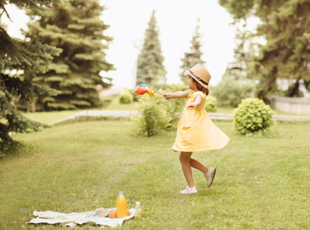 Cute smiling happy little girl in a hat having fun in park meadow. Picnic on nature.の写真素材