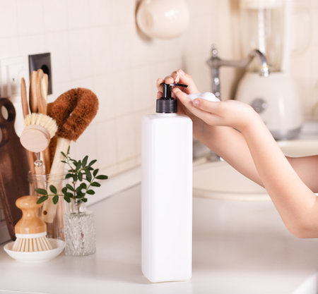 Little kid child washing hands with soap dispenser in a kitchen. Mock-up white container.の写真素材