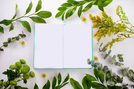 Notebook, card mock up on with green plant and flowers. Space for text. Top view. Greetings templateの写真素材
