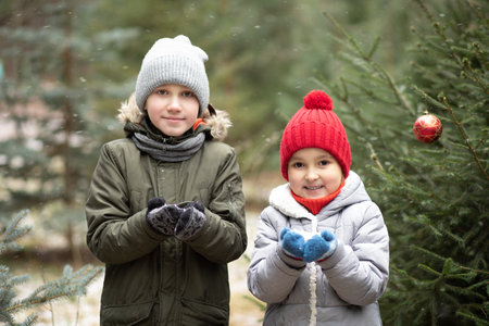 Happy kids girl and boy playing outdoor in snowy winter forest and blowing snow. Active winter holidays celebrate concept. Happy childhoodの写真素材