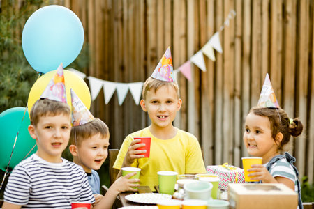 Cute funny nine year old boy celebrating his birthday with family or friends with homemade baked cake in a backyard. Birthday party. Kids wearing party hats and clink paper caps with juiceの写真素材