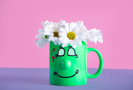 Bouquet of chamomile in green cup with funny face. Greeting postcard.の写真素材