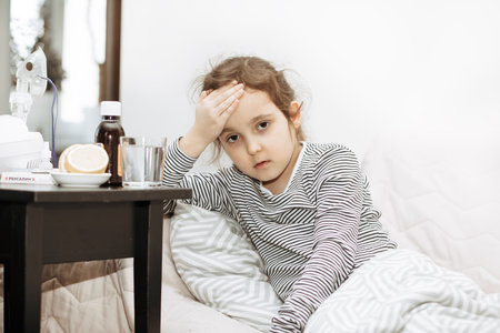 Sick sad little kid girl sits on bed at home. Asthma medicine. Flu season. Healthcare conceptの写真素材