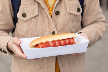 Cute little girl eating hot dog nearby food track on a street.の写真素材