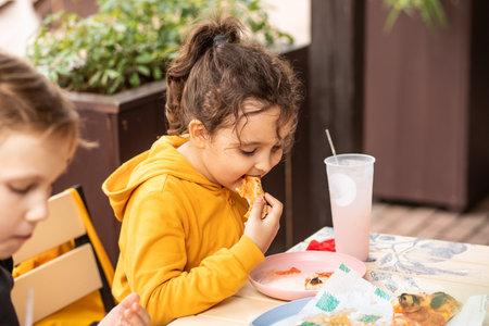 Cute girl and teenager boy eat pizza lunch in outdoor cafe and having fun.の写真素材