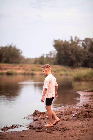 Kid boy teenager walking along the river bank and watches the water. Summer holiday conceptの写真素材