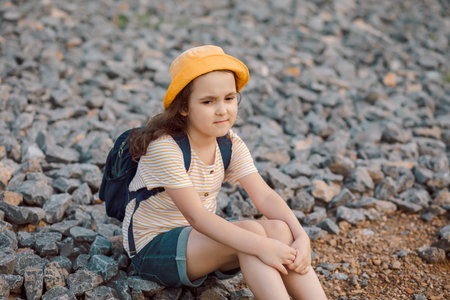 Cute little girl sitting on pebbles at the riverbank looking away.の写真素材