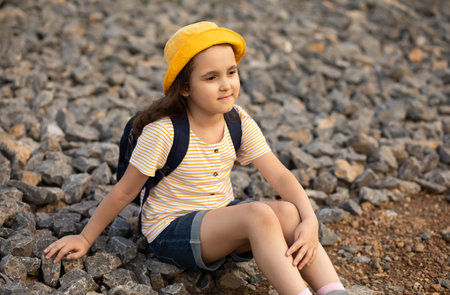 Cute little Girl sitting on pebbles at the riverbank looking away.の写真素材
