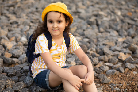 Cute little Girl sitting on pebbles at the riverbank looking away and enjoying summer holiday.の写真素材