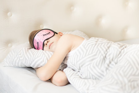 Teenager kid boy in a pink night mask sleeping on bedの写真素材