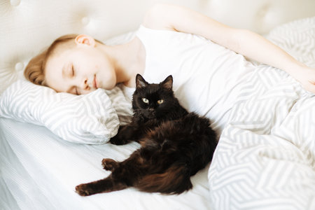 Kid boy teenager sleep on bed with best friend pet black cat.の写真素材