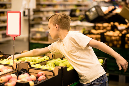 Kid teenager boy shopping for fresh organic fruits apples and vegetables in supermarket.の写真素材