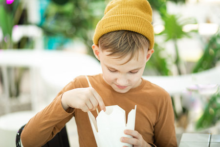 Kid teen child boy eating ramen noodle with chopsticks in food court. Lunch timeの写真素材