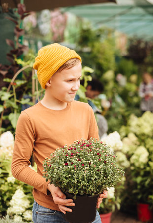 Kid teenager boy buying flowers in a pot. Choosing plants in a local garden centerの写真素材