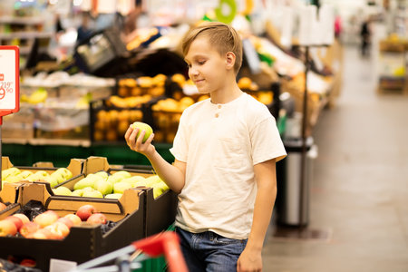 Kid teenager boy shopping for fresh organic fruits apples and vegetables in supermarket.の写真素材