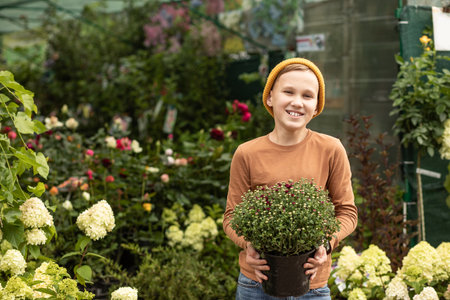 Kid teenager boy buying flowers in a pot. Choosing plants in a local garden centerの写真素材