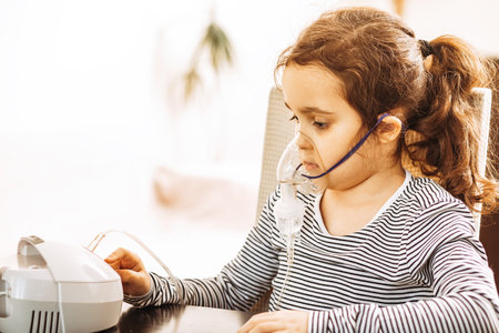 Sick little girl with cough doing inhalation at home with nebulizer inhaler mask. Asthma medicine. Flu season. Healthcare conceptの写真素材