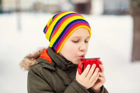 Happy child kid teen boy holding red mug of hot cocoa, chocolate or tea and drinking. Children activity in winter day. Holiday vacation conceptの写真素材