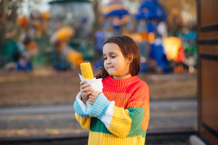 Caucasian little cute girl eating delicious tasty corn on the cob in city parkの写真素材