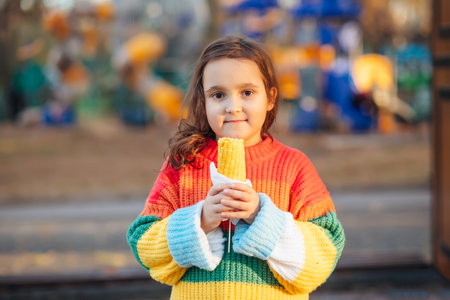Caucasian little cute girl eating delicious tasty corn on the cob in city parkの写真素材