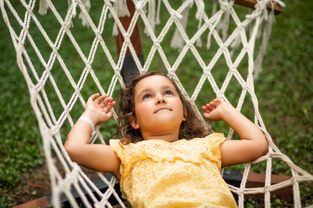 Cute little girl swinging and relaxing in hammock in backyard. Summer kids activityの写真素材