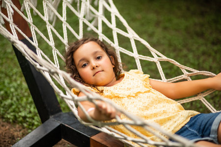 Cute little girl swinging and relaxing in hammock in backyard. Summer kids activityの写真素材