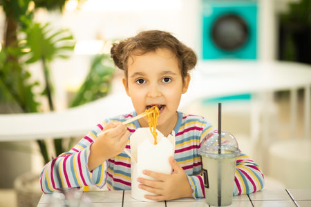 Kid child girl eating ramen noodle wok with chopsticks in food court. Lunch timeの写真素材