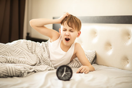 Kid boy teenager waking up yawning and stopping alarm clock in the morning.の写真素材