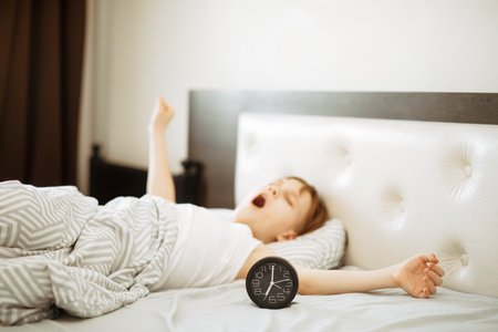 Kid boy teenager waking up yawning and stopping alarm clock in the morning.の写真素材