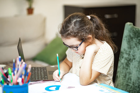 Little cute girl pupil at home making homework. Child studying online on laptop. Kid educationの写真素材