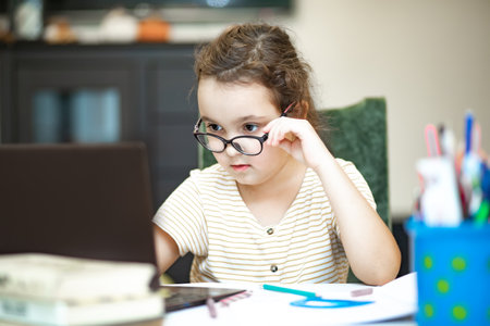 Little cute girl pupil at home making homework. Child studying online on laptop. Kid educationの写真素材