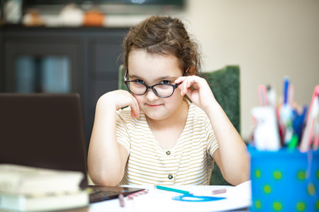 Little cute girl pupil at home making homework. Child studying online on laptop. Kid educationの写真素材