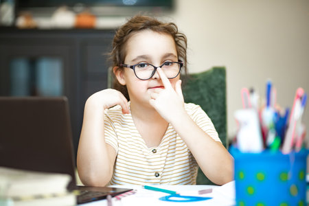 Little cute girl pupil at home making homework. Child studying online on laptop. Kid educationの写真素材