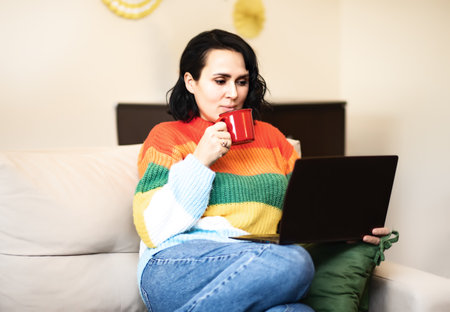 Woman 40s using a laptop working from home in living room. Alternative office freelance conceptの写真素材