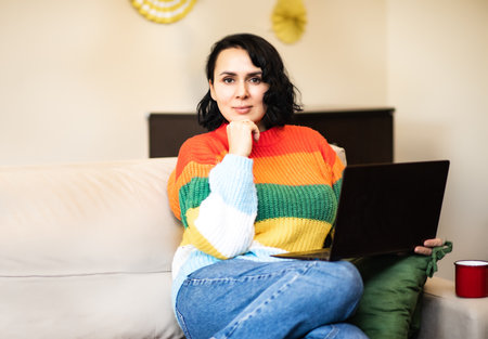 Woman 40s using a laptop working from home in living room. Alternative office freelance conceptの写真素材