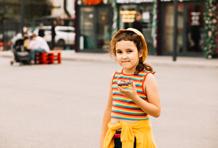 Kid little girl eating colorful sweet and tasty donuts. Child snacking on unhealthy food outdoors. Food delivery or take away food concept.の写真素材