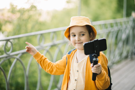 Cute little girl in yellow hat taking selfie with mobile phone outdoor in a park. Kid blogger recording video vlog.の写真素材