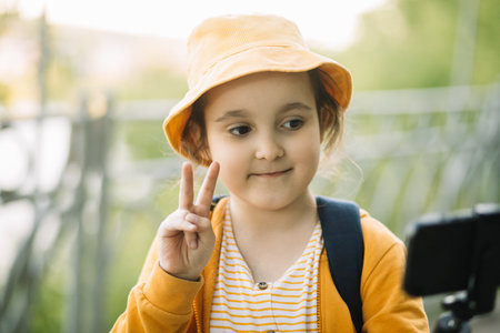 Cute little girl in yellow hat taking selfie with mobile phone outdoor in a park. Kid blogger recording video vlog.の写真素材